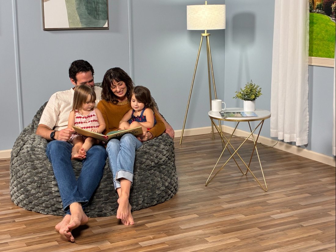 A family of four sits on a cordaroys bean bag in a living room. 