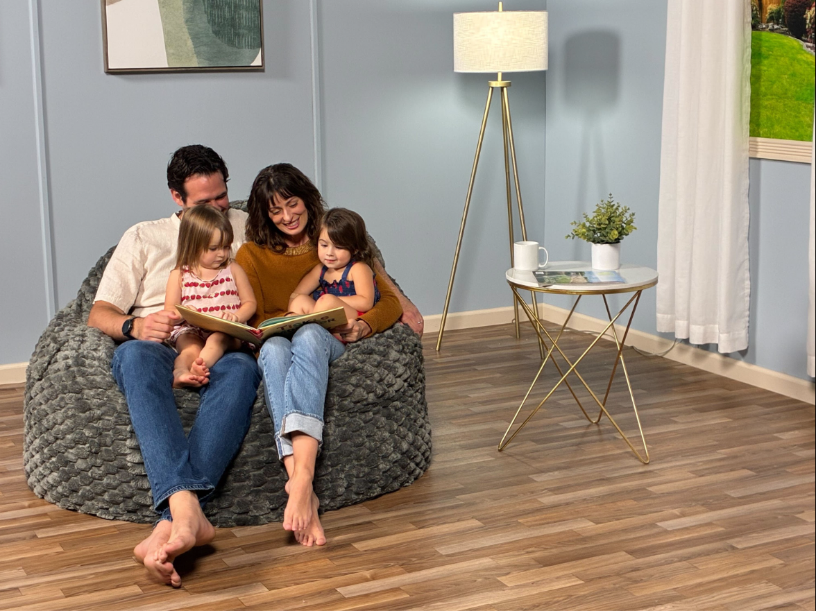 A family of four sits on a cordaroys bean bag in a living room. 