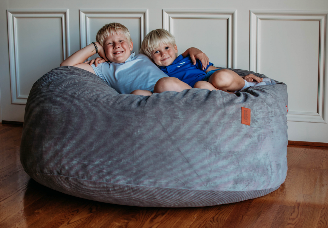 Two kids lay on a cordaroys bean bag chair. 