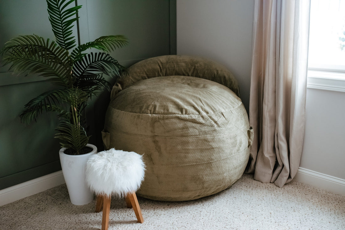 A cordaroys bean bag in the corner of an apartment living room next to a plan and footstool. 