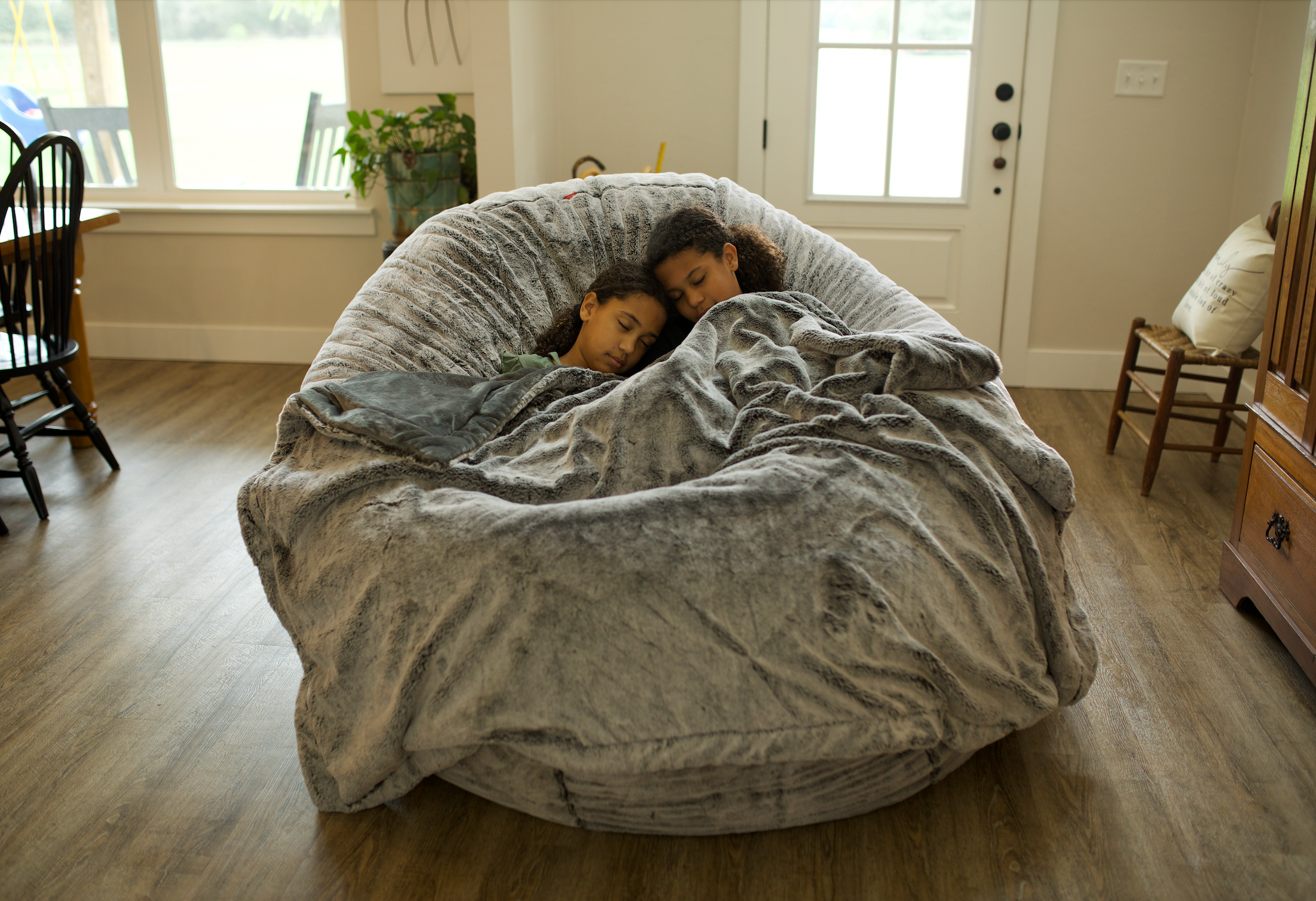 Two children sleeping on a large CordaRoy's bean bag chair. 