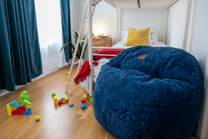 A CordaRoy's Bean Bag sits in a room with toys and a bunk bed. 