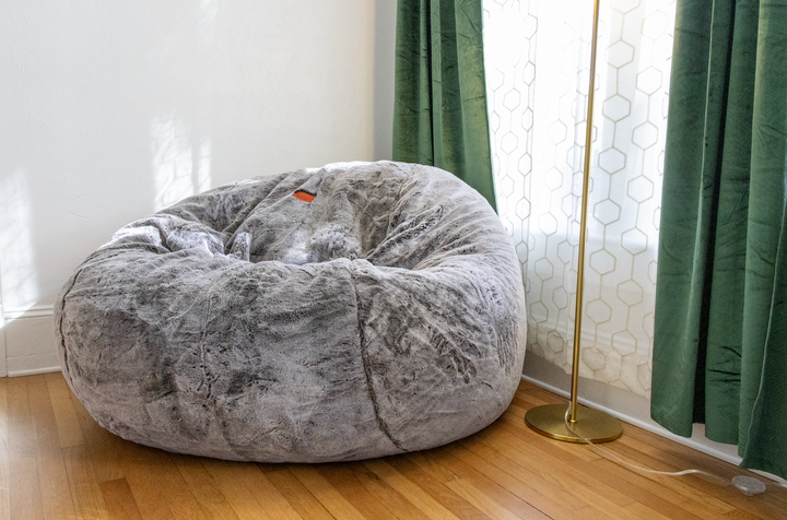 A CordaRoy's Bean Bag in the corner of a living room in front of a window. 