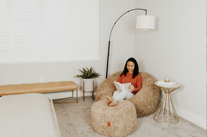 A women sits on a CordaRoy's bean bag with a pouf. 