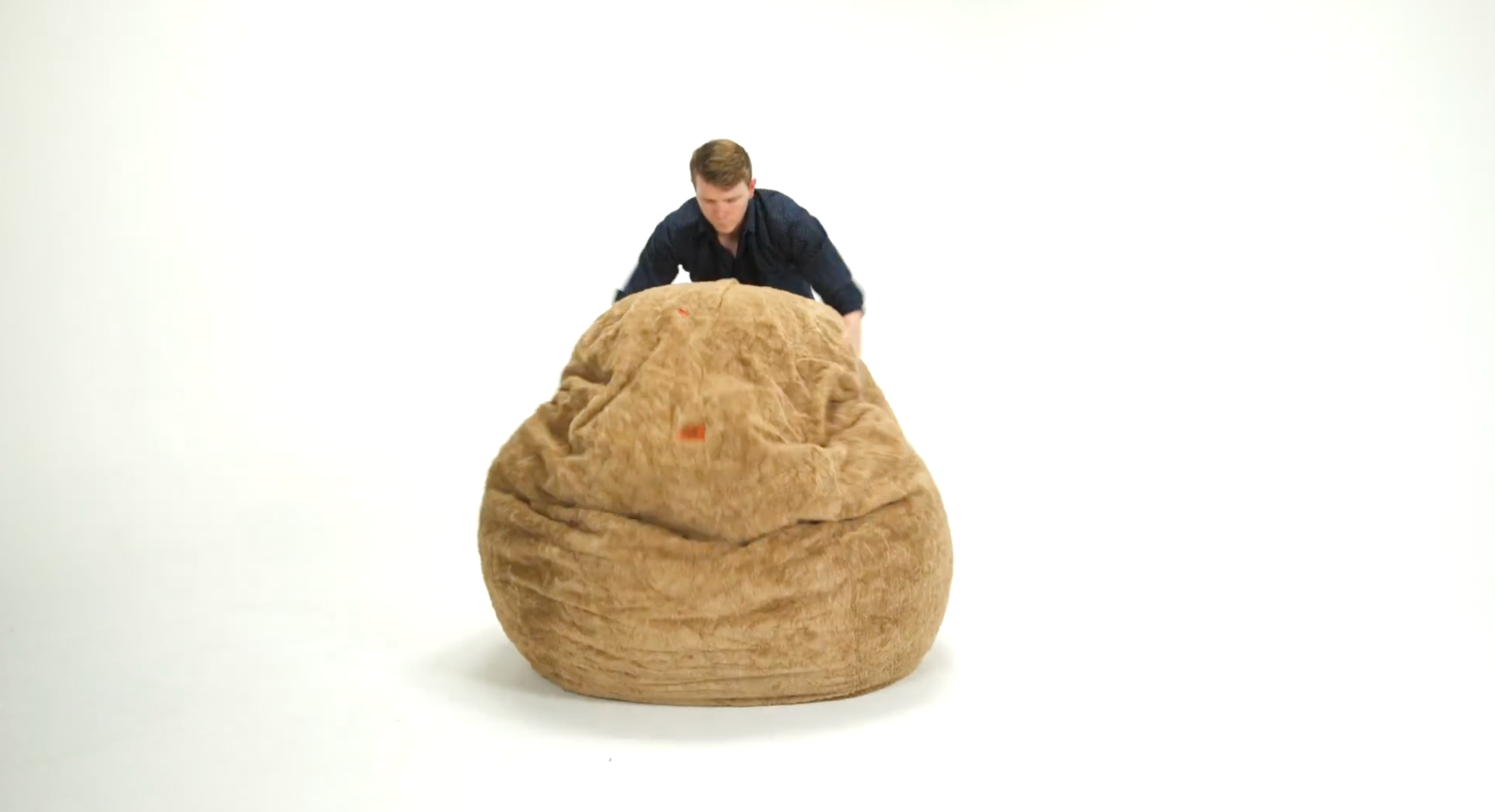 A man demonstrating how to fluff a flat bean bag chair. 