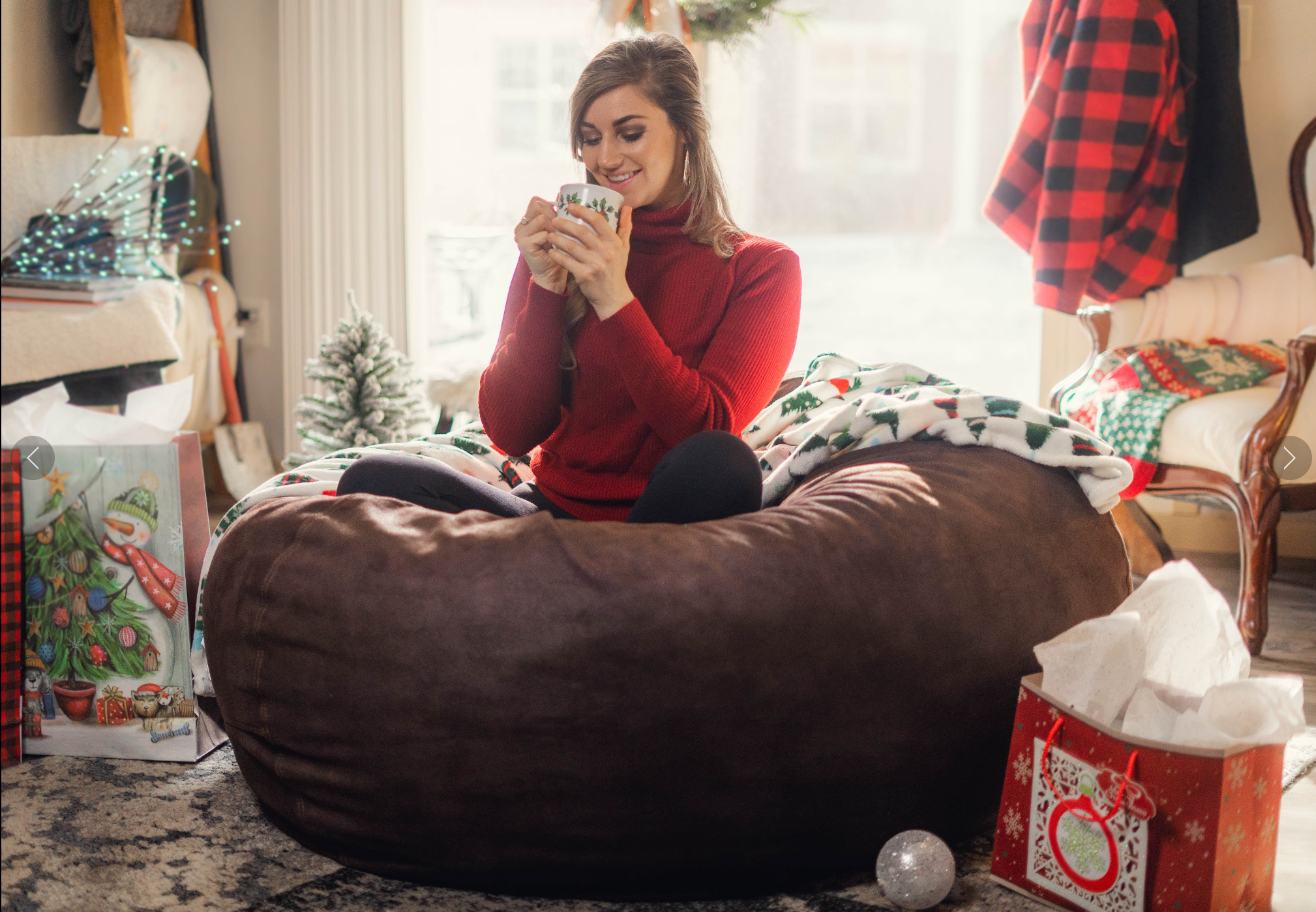 A woman sits on a bean bag chair in her living room surrounded by holiday decor.