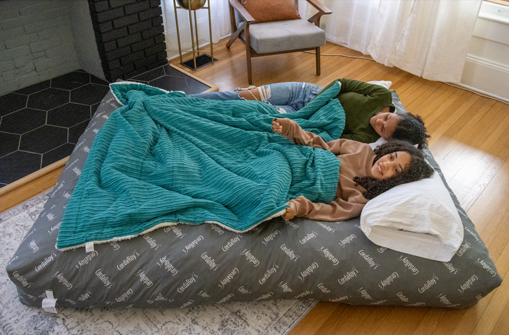 Two people sleeping on a CordaRoy's bean bag chair in bed form. 