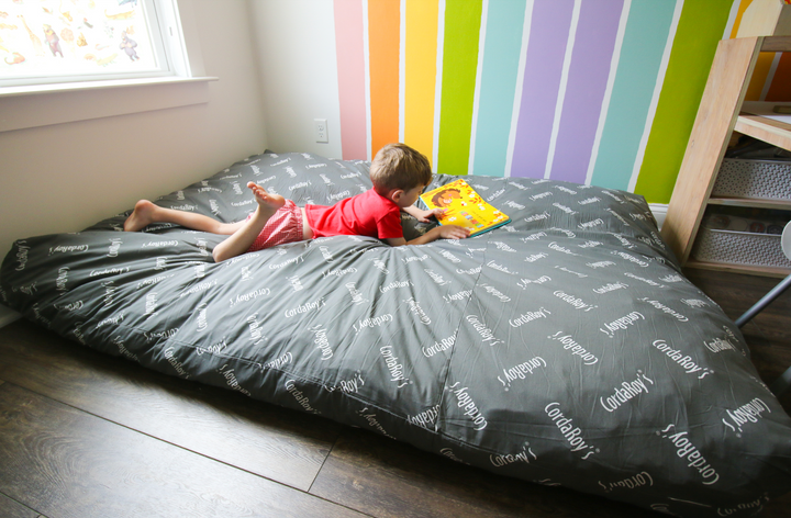 A child sits on a CordaRoy's Bean Bag expanded in bed form in front of a rainbow wall.