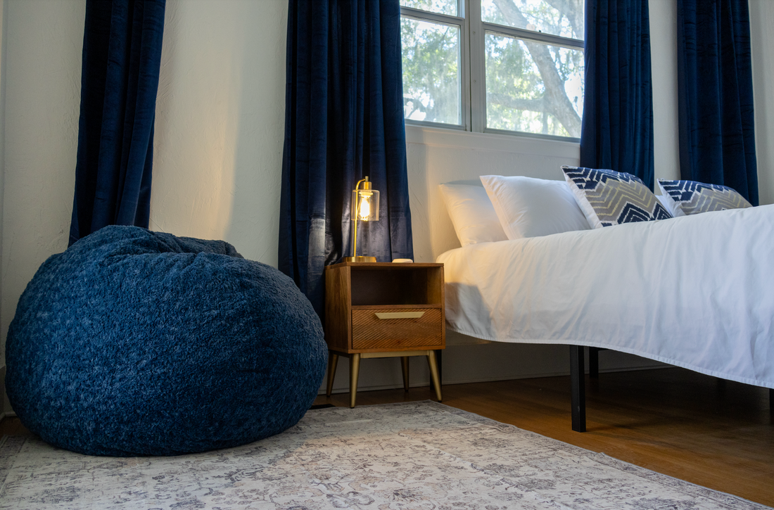 A bean bag chair in the corner of a room with a nightstand and a bed. 