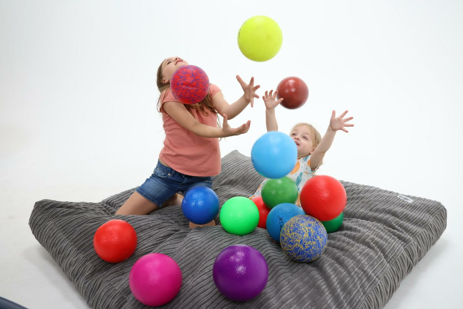 Two girls play with balls on a cordaroys bean bag bed