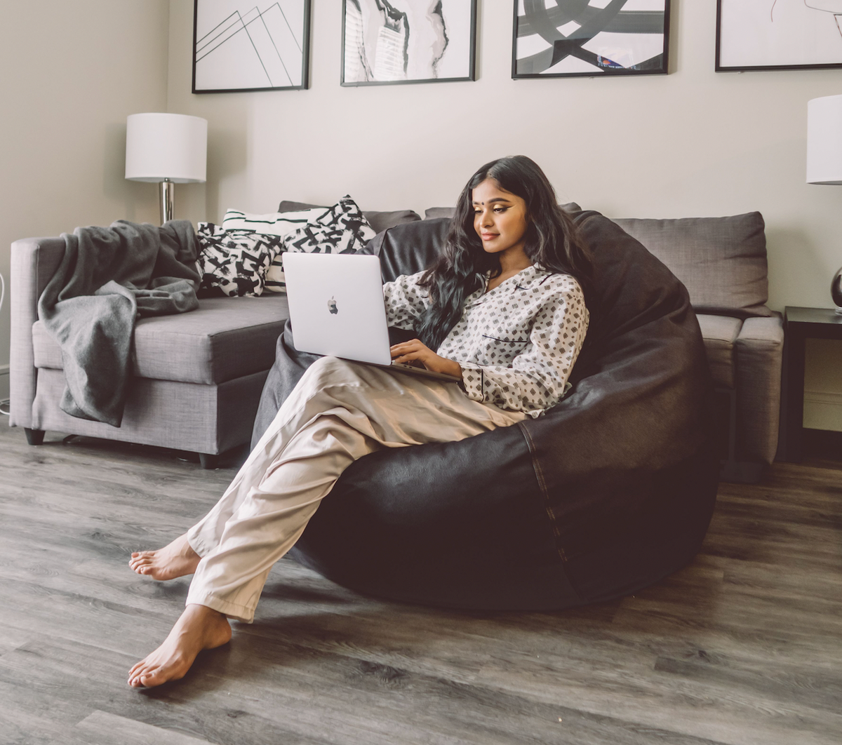 A woman working on a laptop while sitting on a CordaRoy's Bean Bag Chair. 