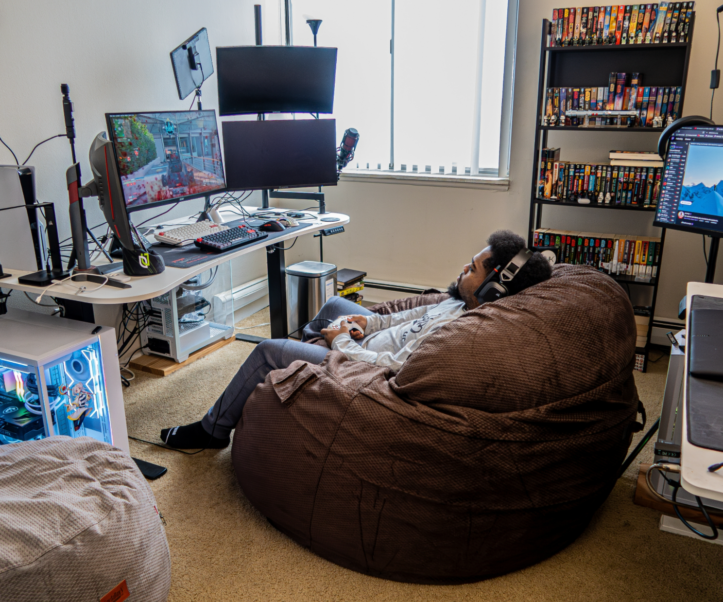 A person playing a computer game while sitting in a cordaroys bean bag surrounded by desks. 