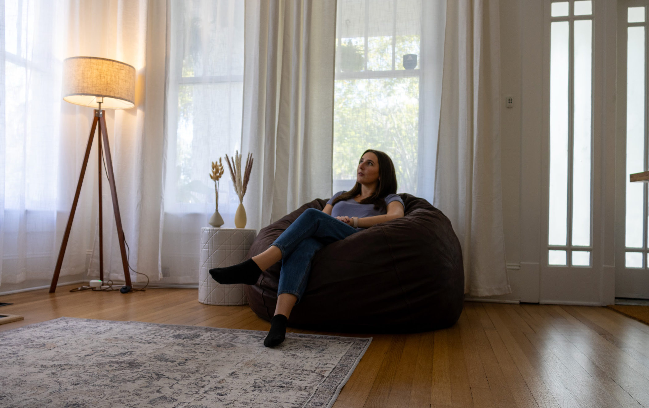 A woman sits in a cordaroys bean bag chair in the corner of a living room.