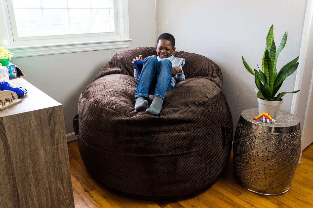 A child sits in a cordaroys bean bag and plays on a tablet. 