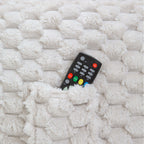 Black remote control with colorful buttons inside a bean bag pocket on a textured white surface