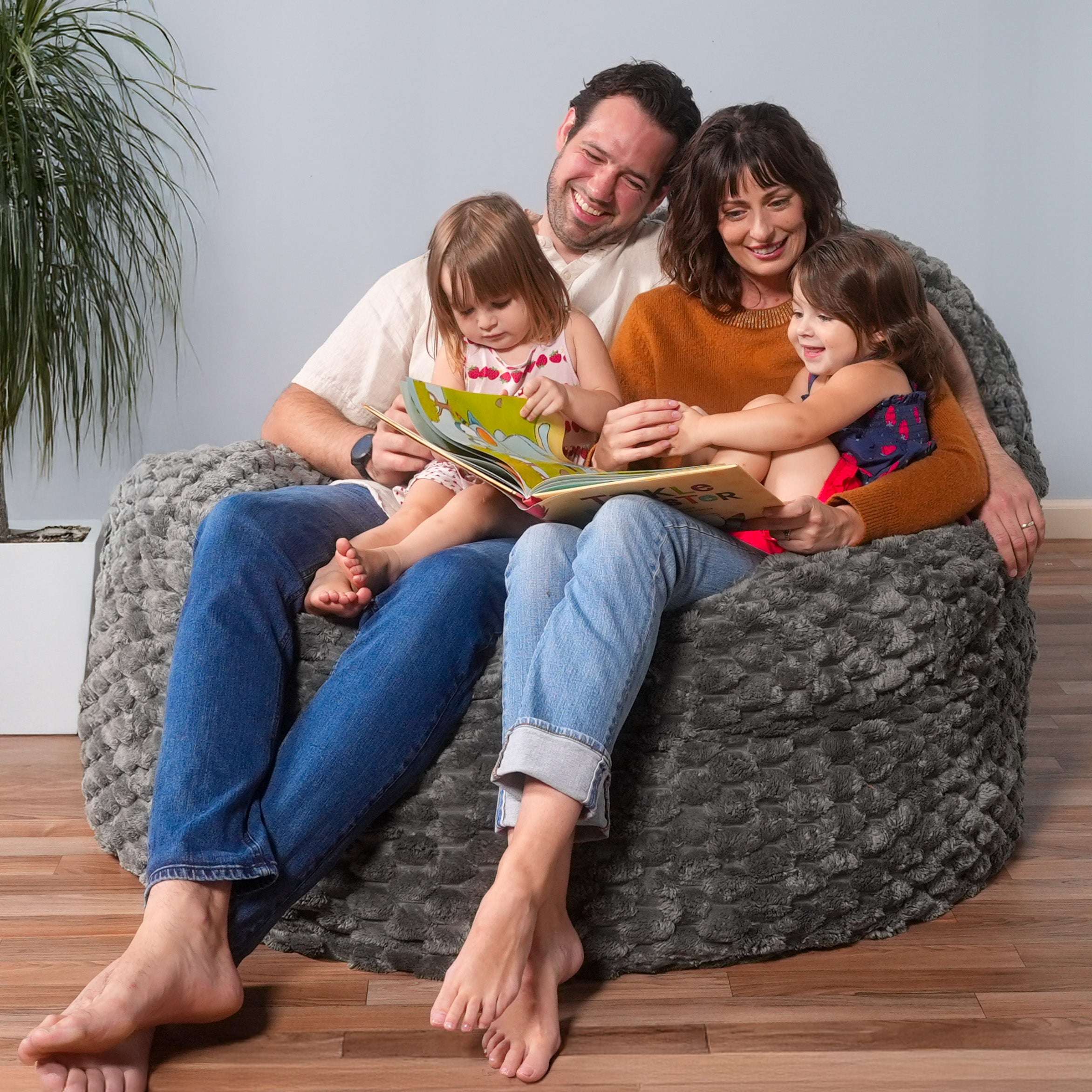 Family of four sitting on a bean bag chair reading together.