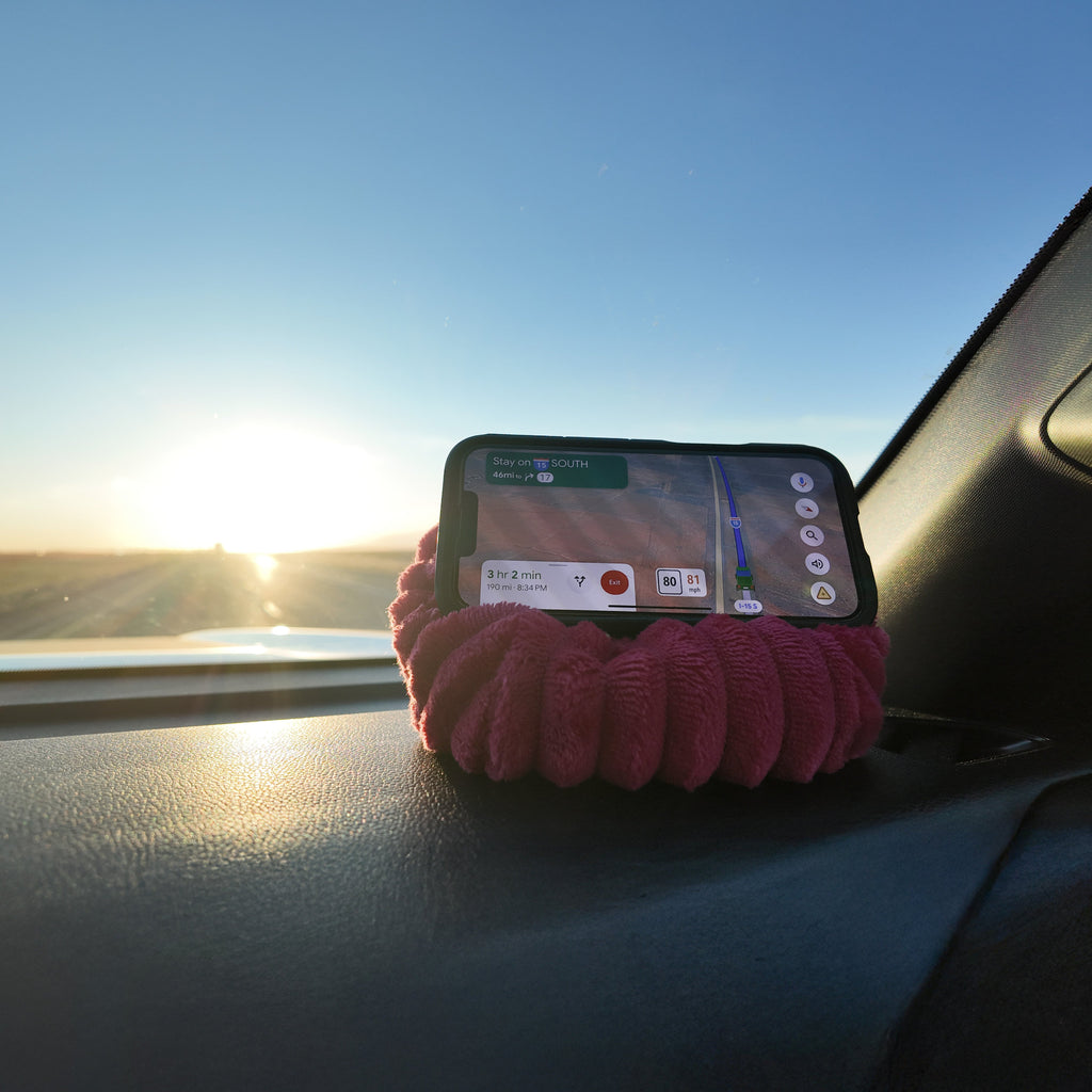 Phone on a pink bean bag with a scenic view outside a car window.