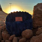 Dark blue indigo bean bag resting on rocks with a scenic sunset.