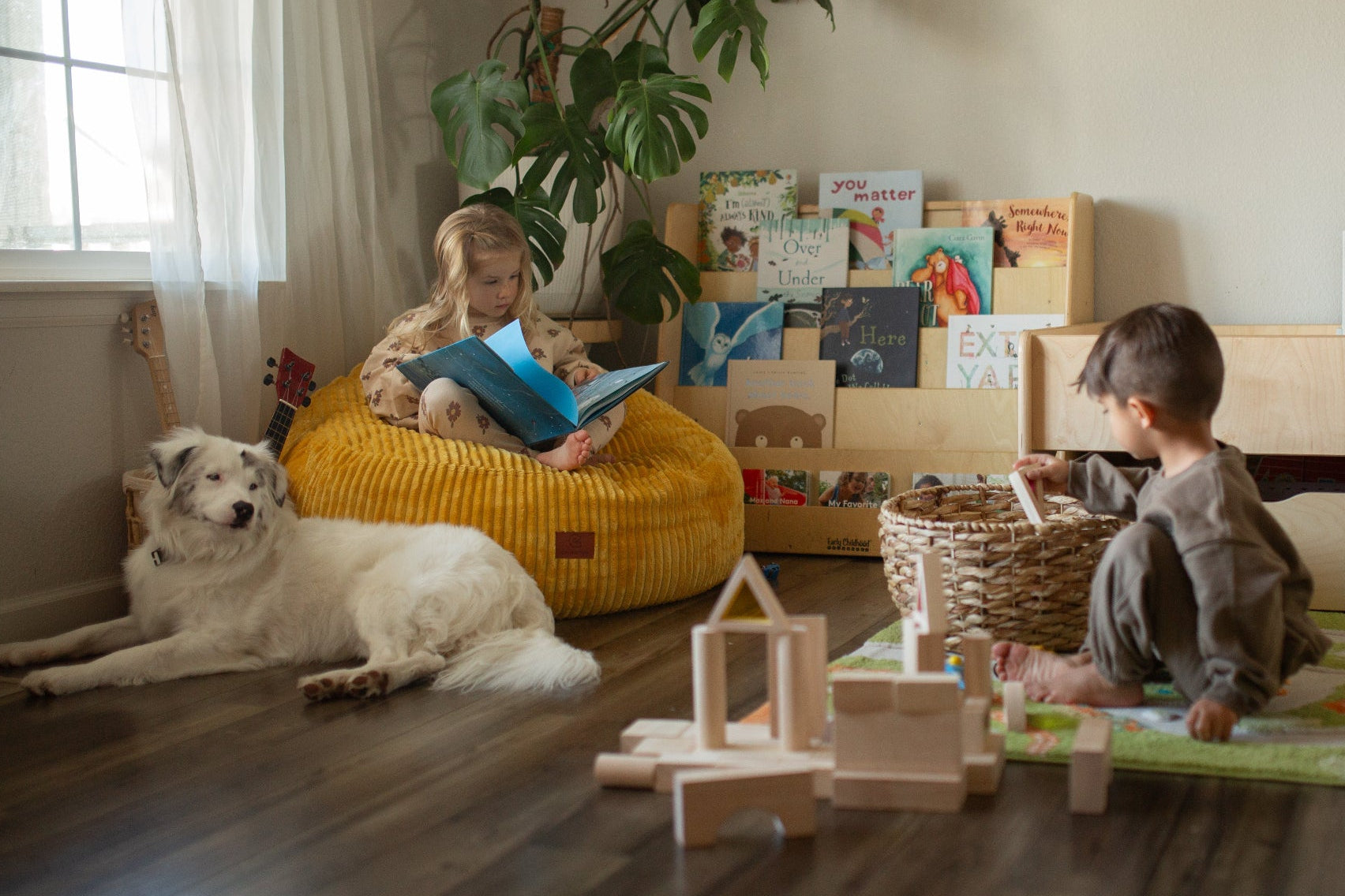 Two children playing with toys on a wooden floor in a room with a dog and books.