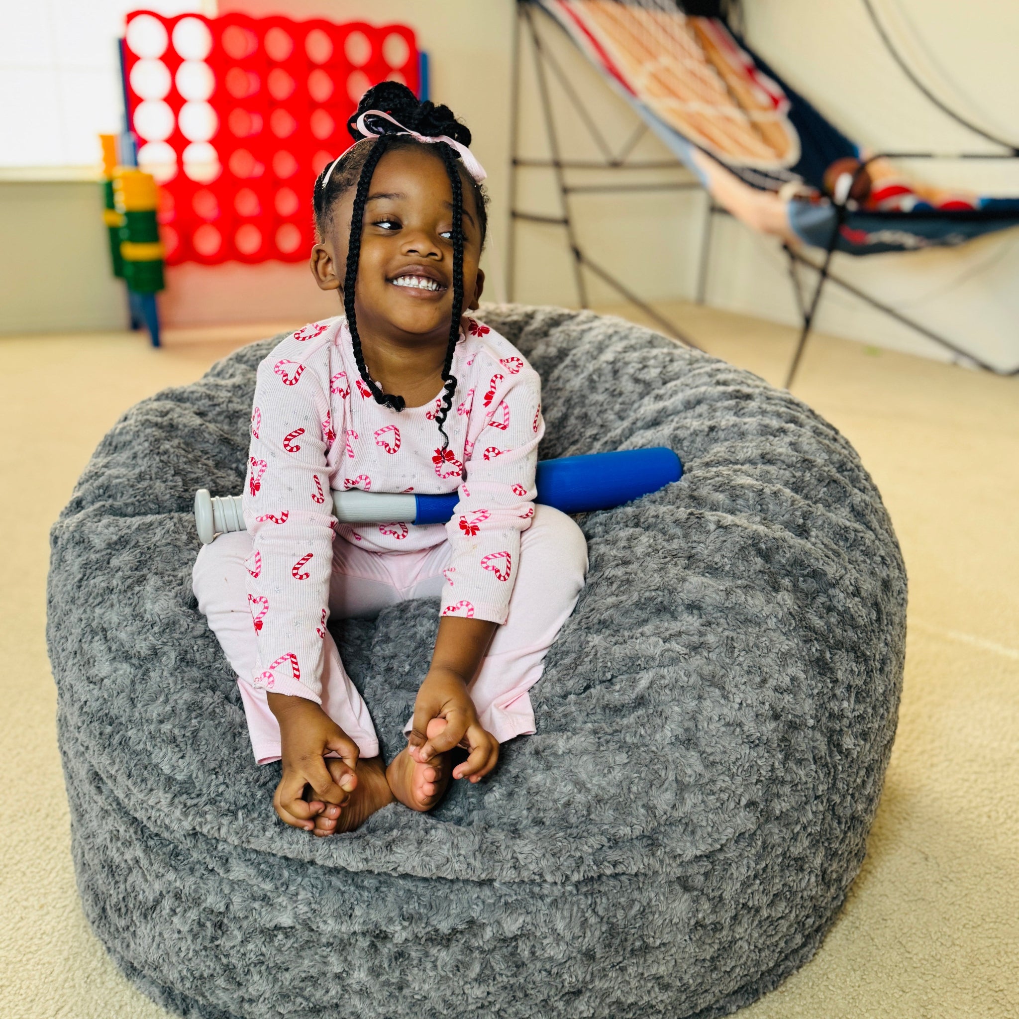 Child sitting on a gray bean bag chair in a room with colorful toys and furniture.