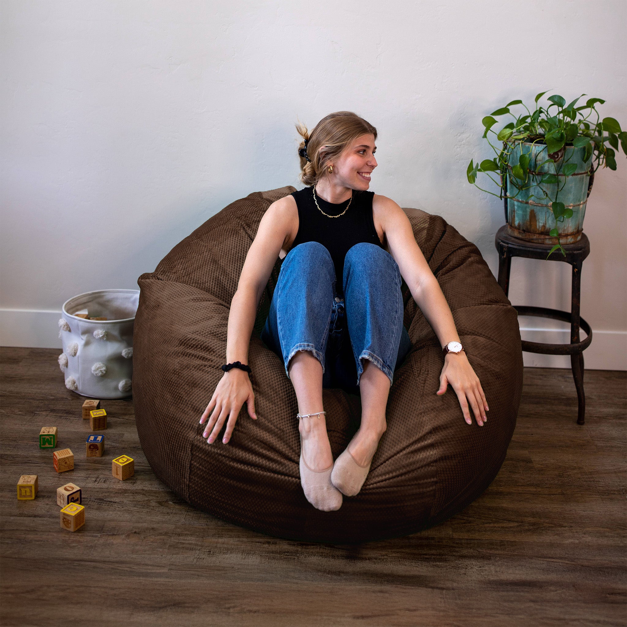 Woman sitting on a brown bean bag chair in a room with toys and plants.