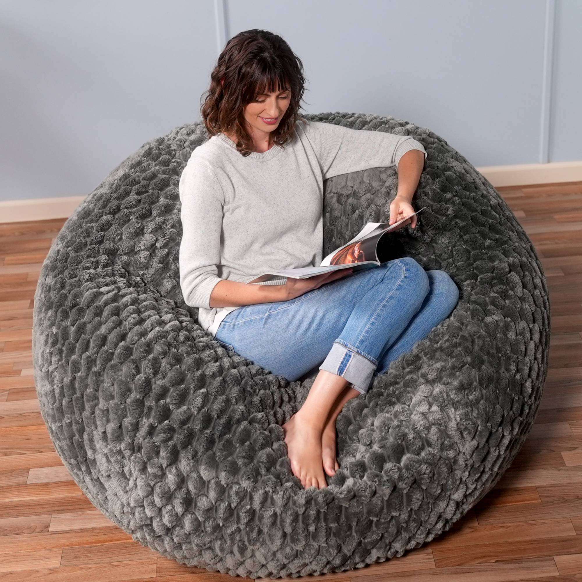 Woman reading a book on a large gray textured bean bag chair.