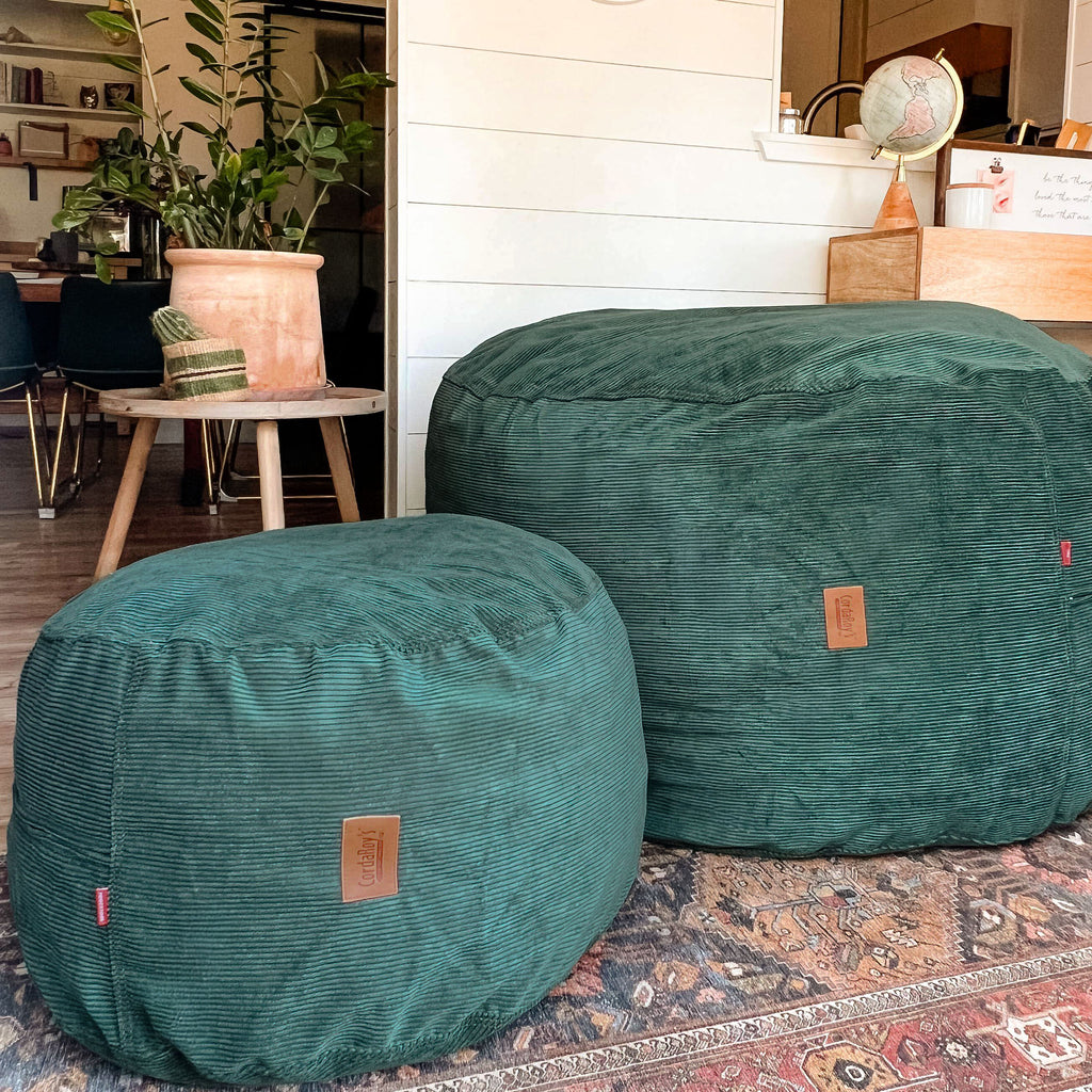 Two green textured ottomans on a patterned rug with a room in the background.