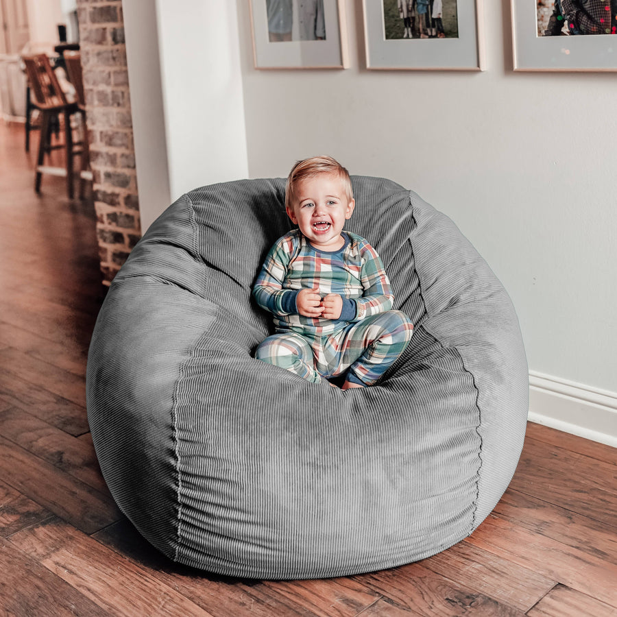 A toddler sits in a gray cordaroy full bean bag chair. 