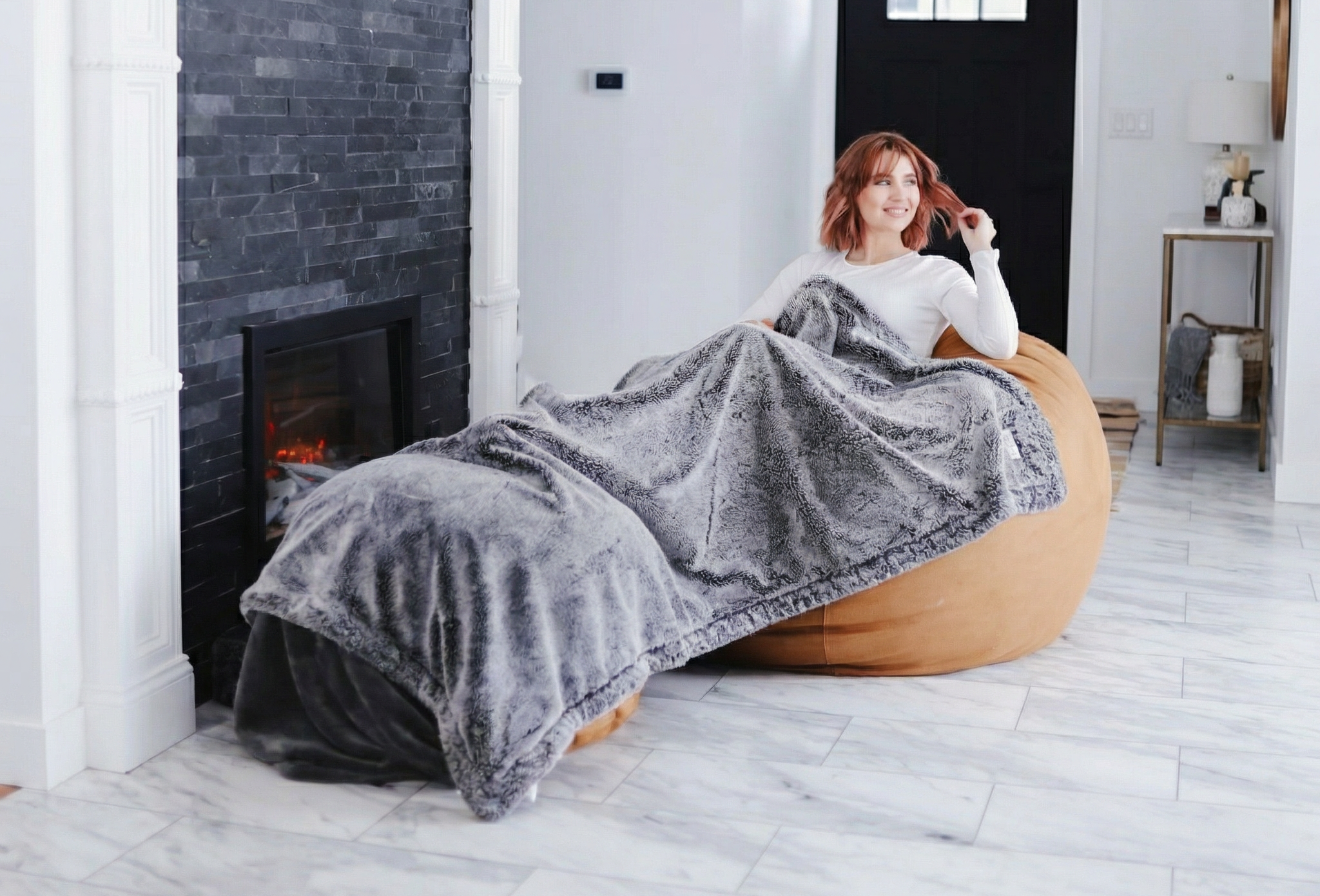 Woman sitting on a bean bag chair with a gray blanket in a modern living room.