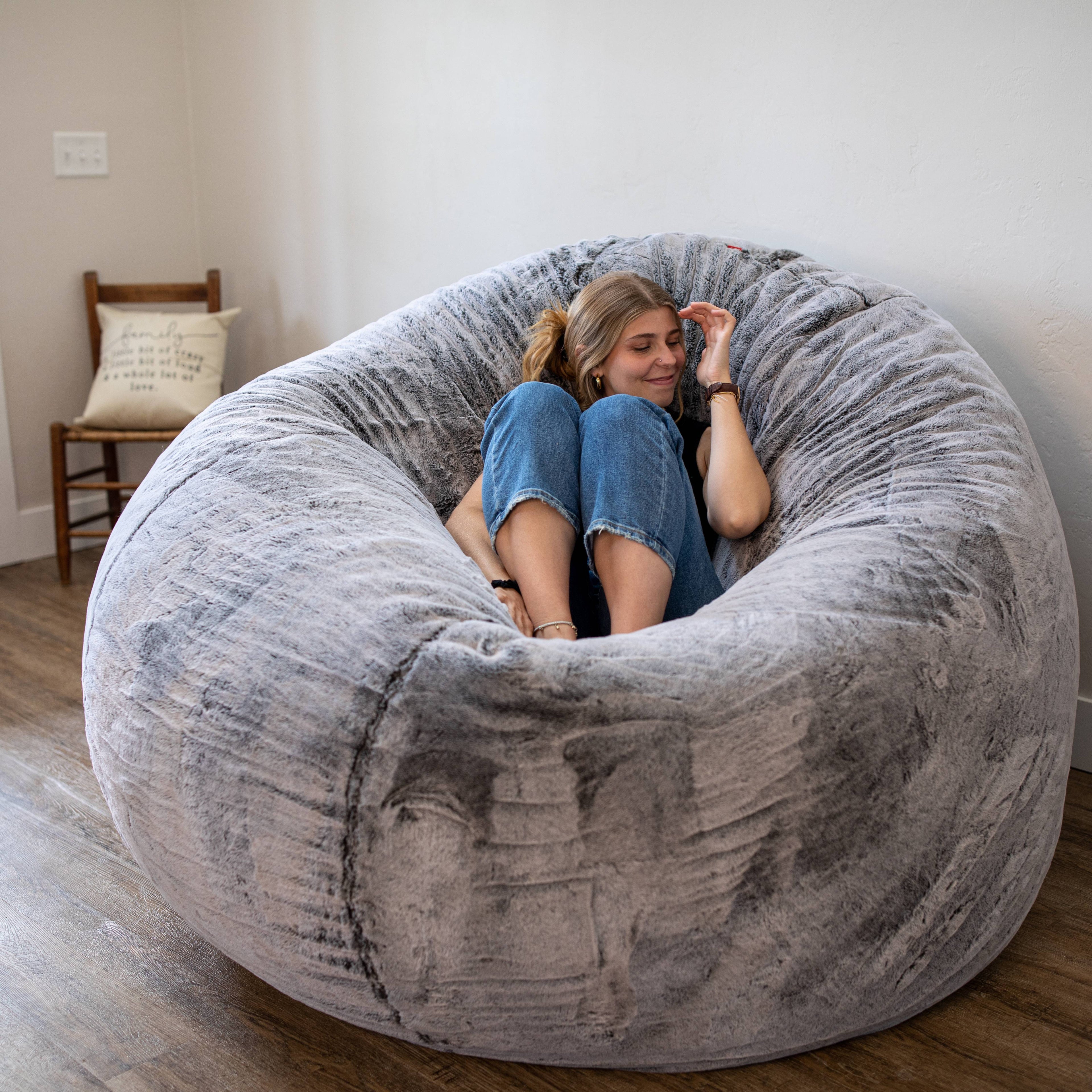 A woman sits on a cordaroys chinchilla giant bean bag chair.