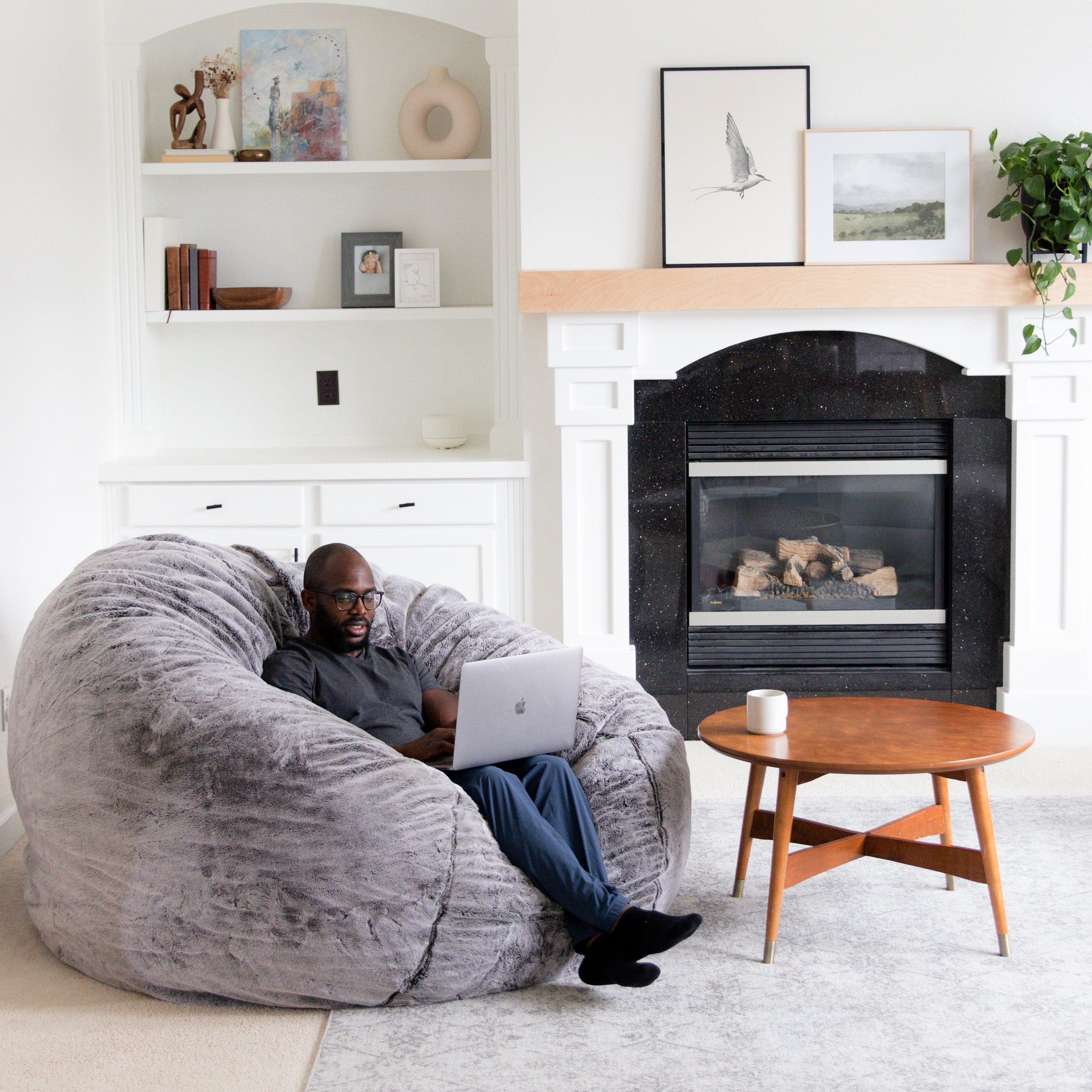 A man sits on a giant bean bag iin chinchilla on a laptop in his living room. 