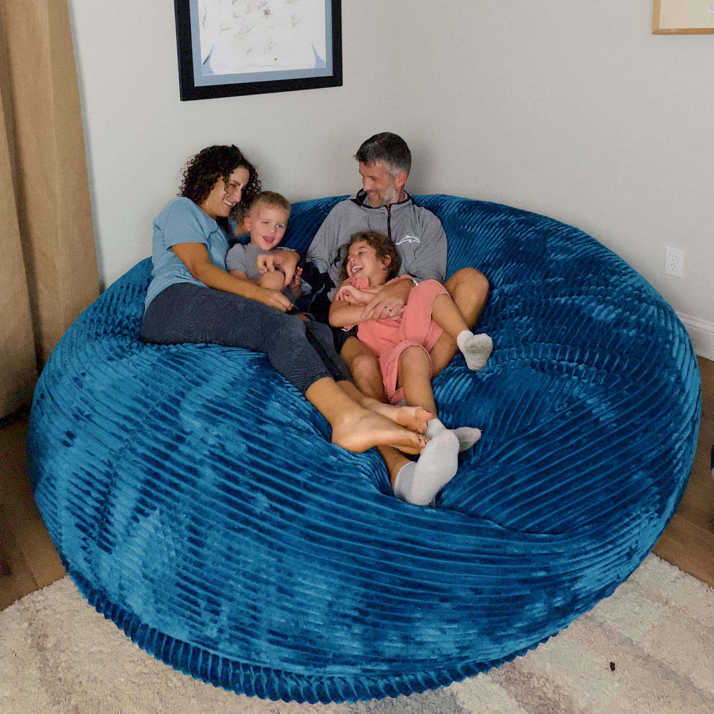 A family of four sits on a cordaroys plush corduroy giant bean bag chair. 