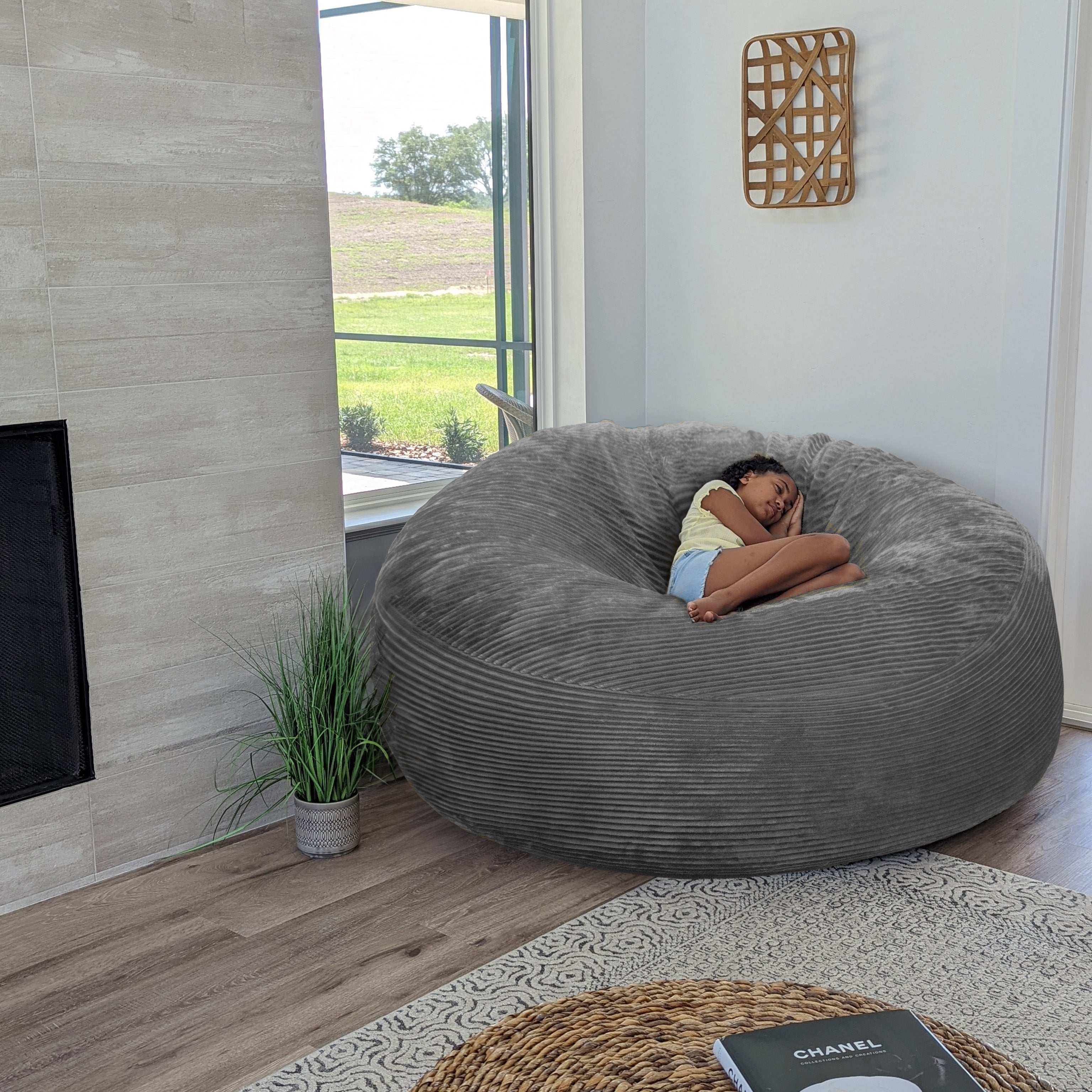 A girl sits on a cordaroys plush corduroy giant bean bag chair in gray. 