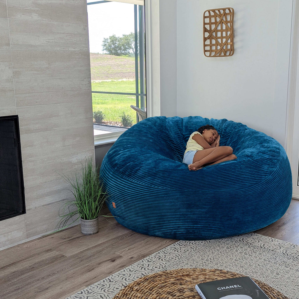 A girl sits on a cordaroys plush corduroy giant bean bag chair in ocean. 