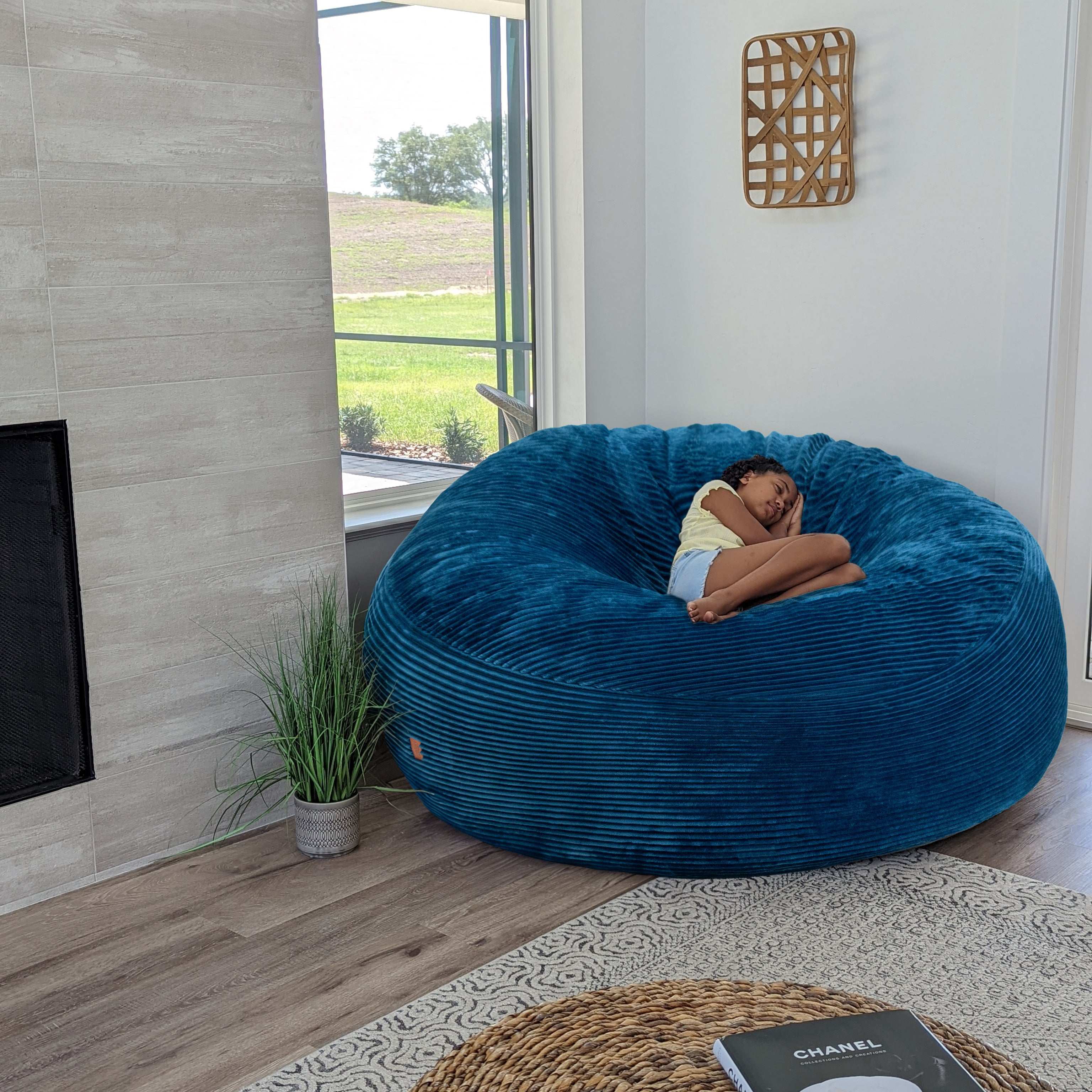 A girl sits on a cordaroys plush corduroy giant bean bag chair in ocean. 
