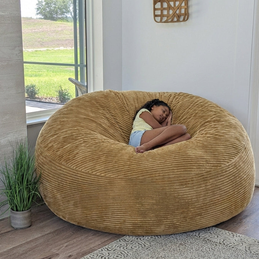 A girl sits on a cordaroys plush corduroy giant bean bag chair in tan. 