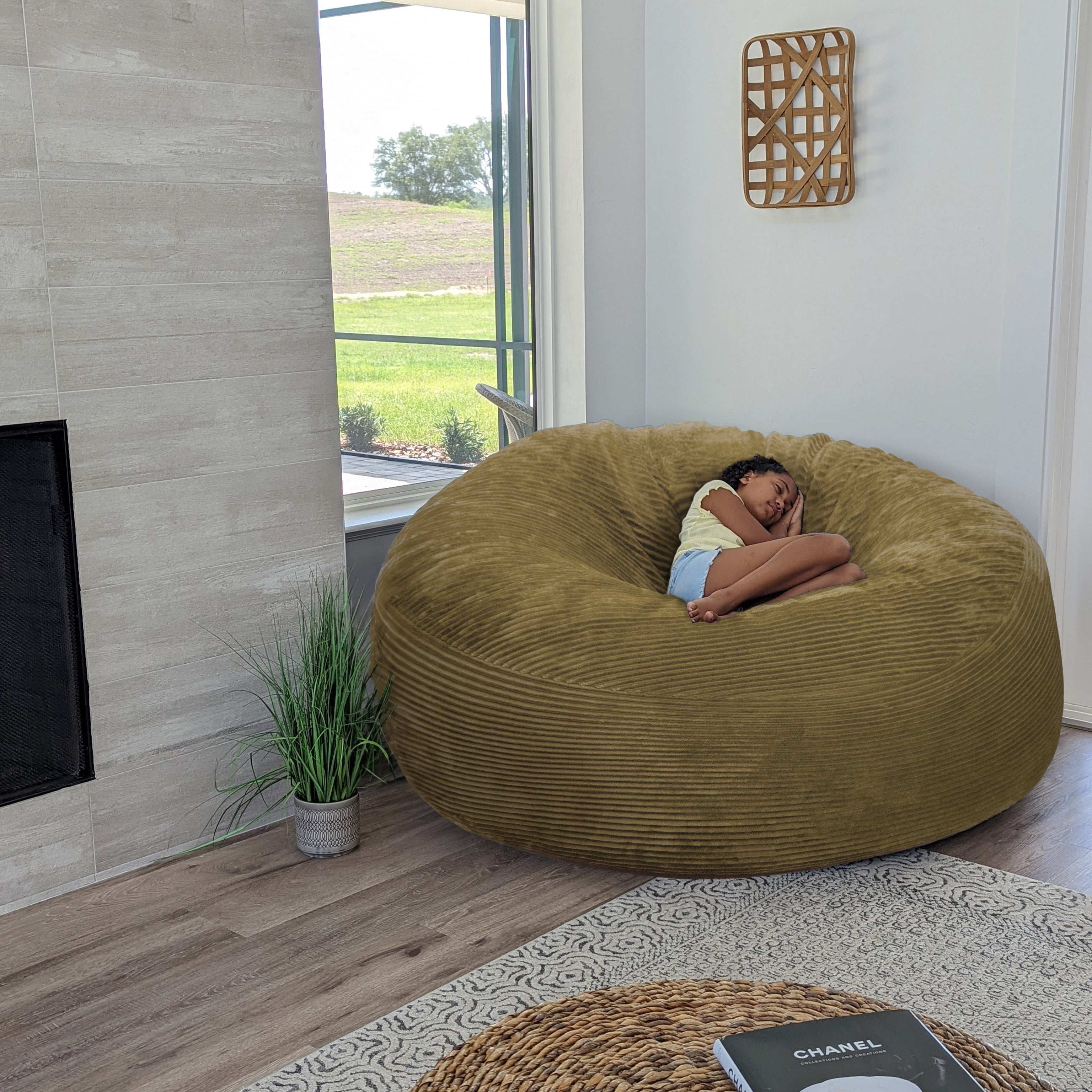 A girl sits on a cordaroys plush corduroy giant bean bag chair in tan. 
