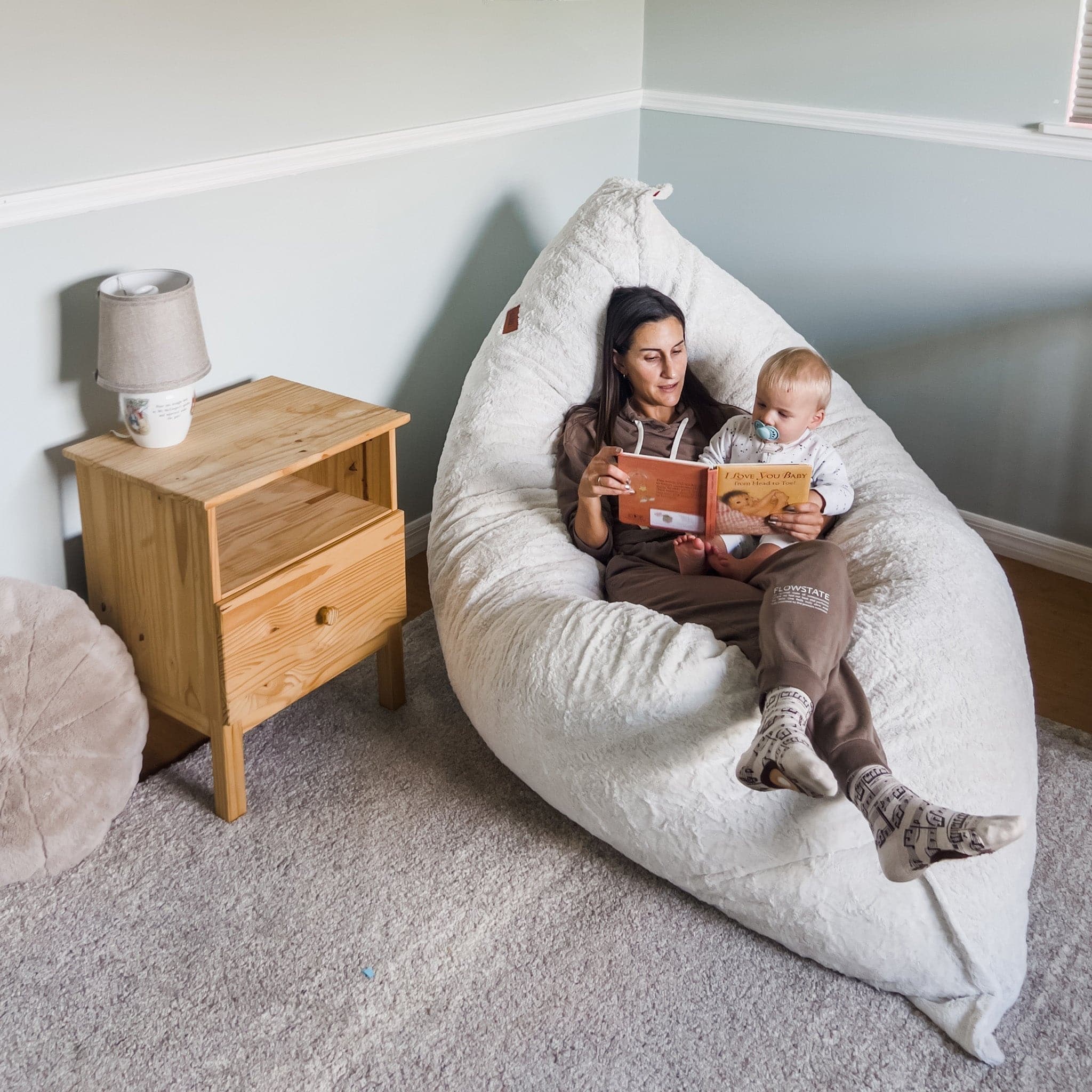 A mom reads a book to her child in a cordaroys giant pillow lounger. 