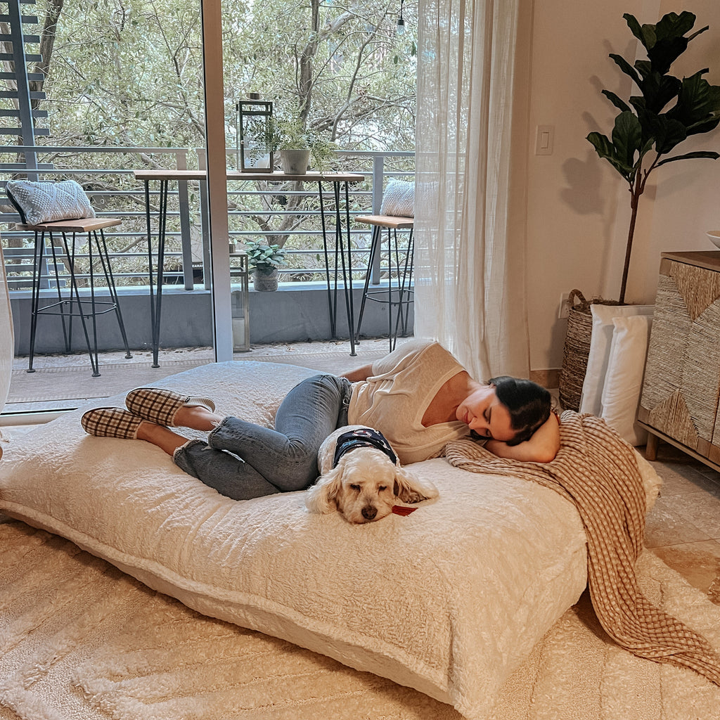 A woman and her dog lie on a flat cordaroys pillow lounger.
