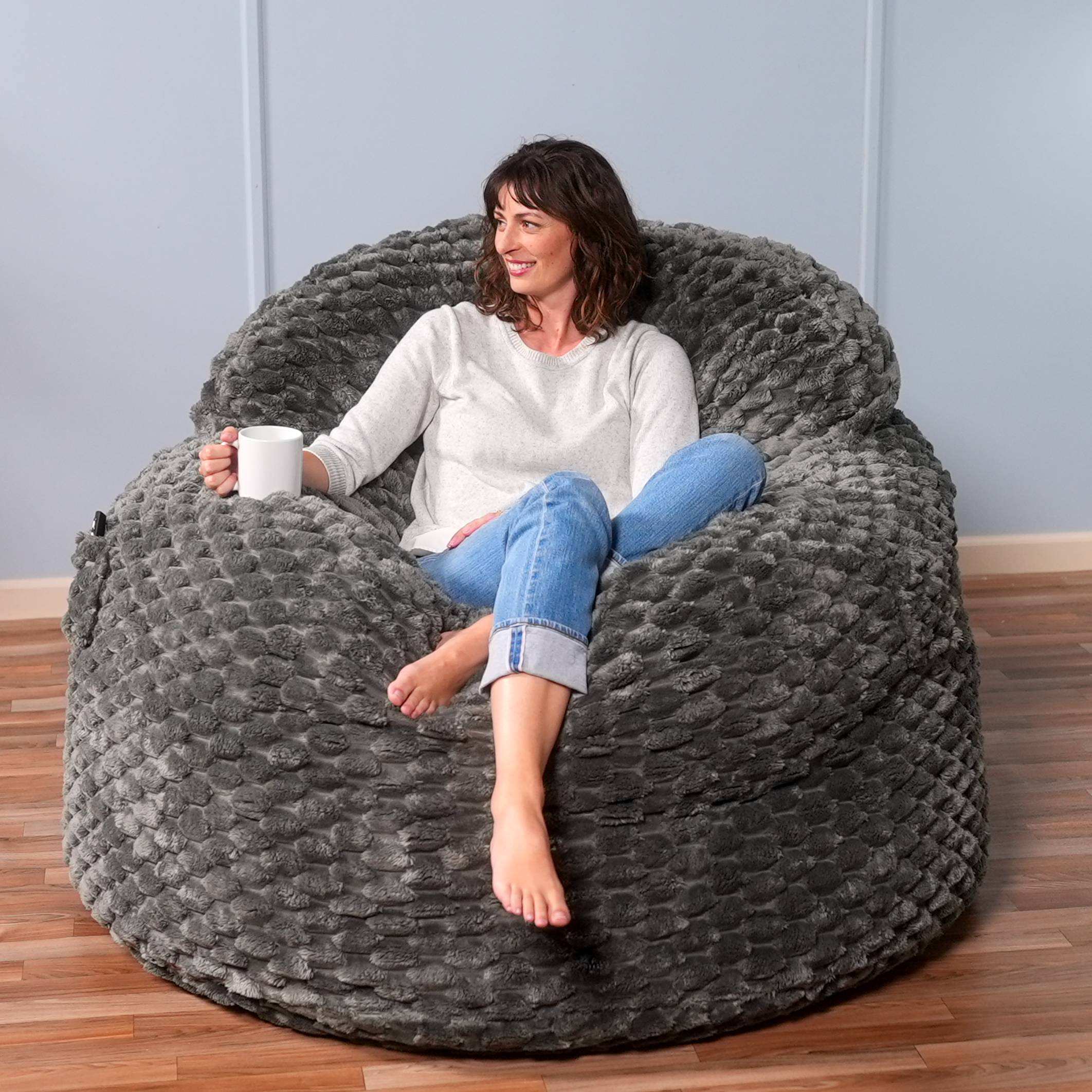 Woman sitting on a large gray textured bean bag chair holding a white mug.