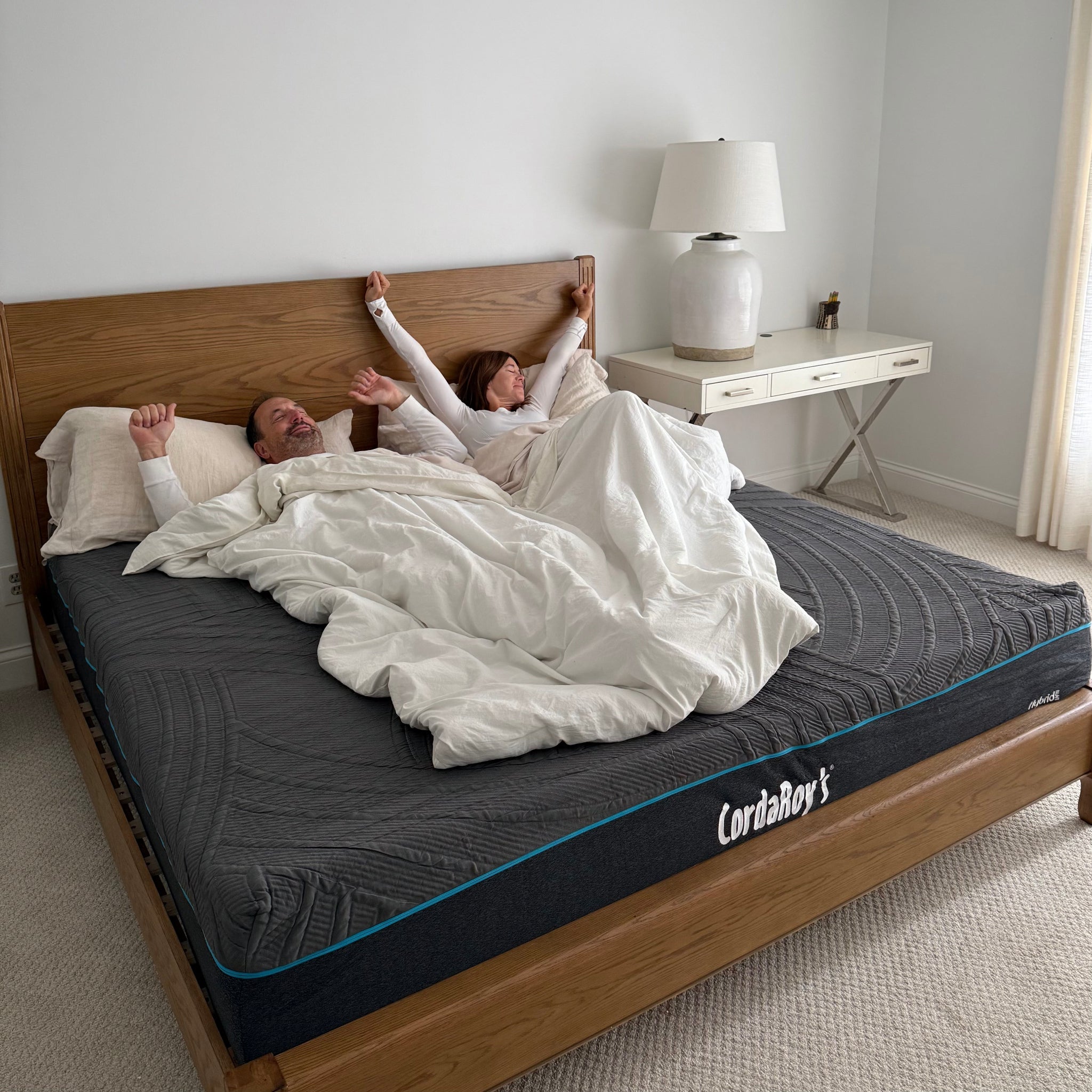 Two people lying in bed under a white comforter with a CordaRoy's mattress visible.