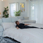A woman lies on a cordaroys king chinchilla bean bag in bed form in a living room.
