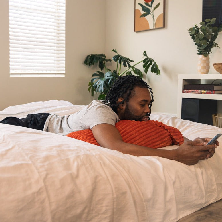 A man lays on an expanded king cordaroys bean bag while on his phone. 