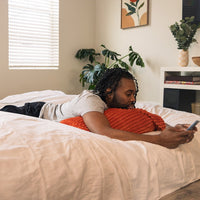 A man lays on an expanded king cordaroys bean bag while on his phone. 