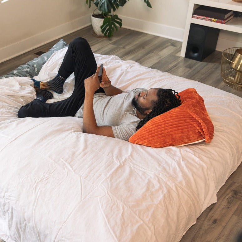 A man sits on a king sized cordaroys Chinchilla bean bag in bed form. 