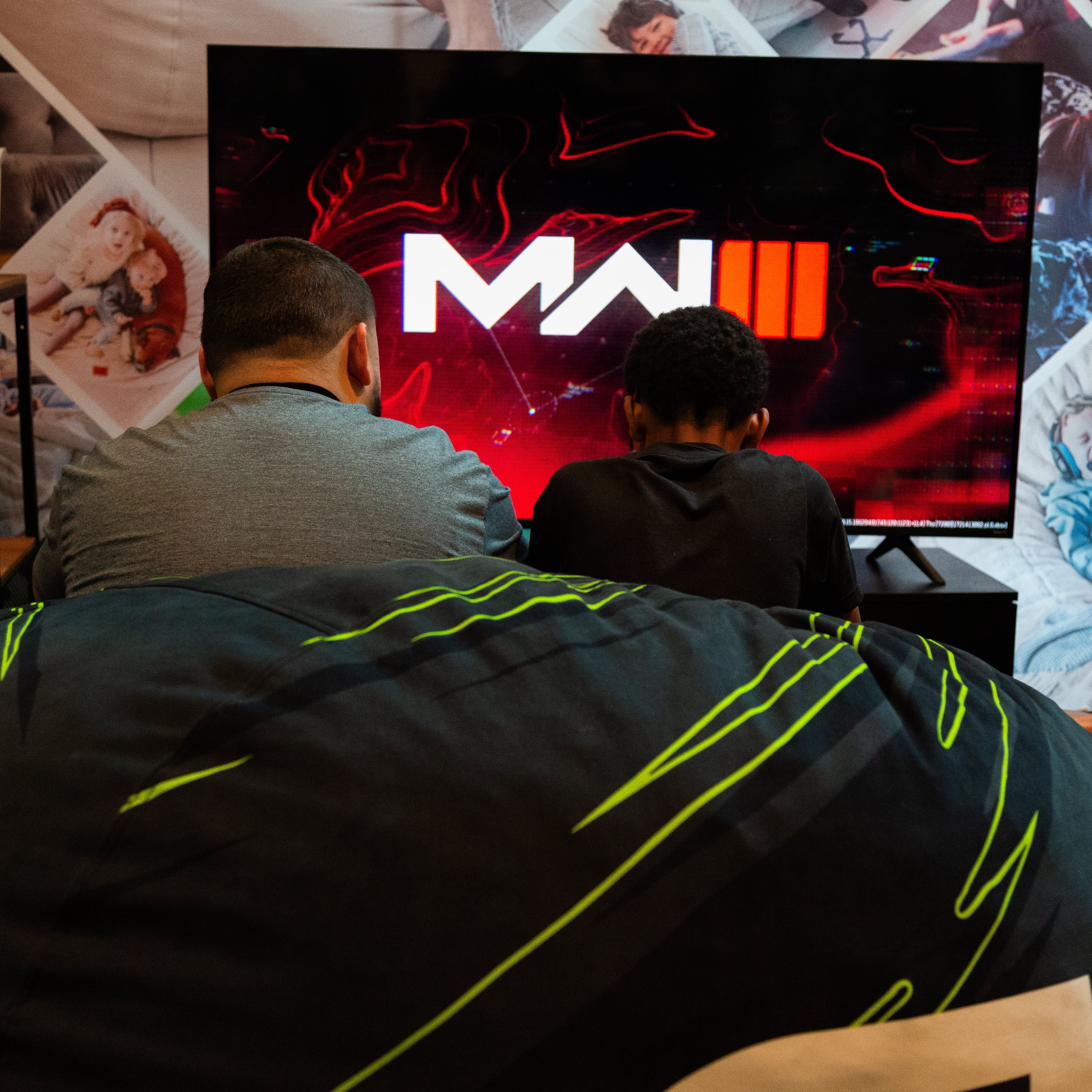 Father and son gaming in front of a television screen displaying a logo with the letter.