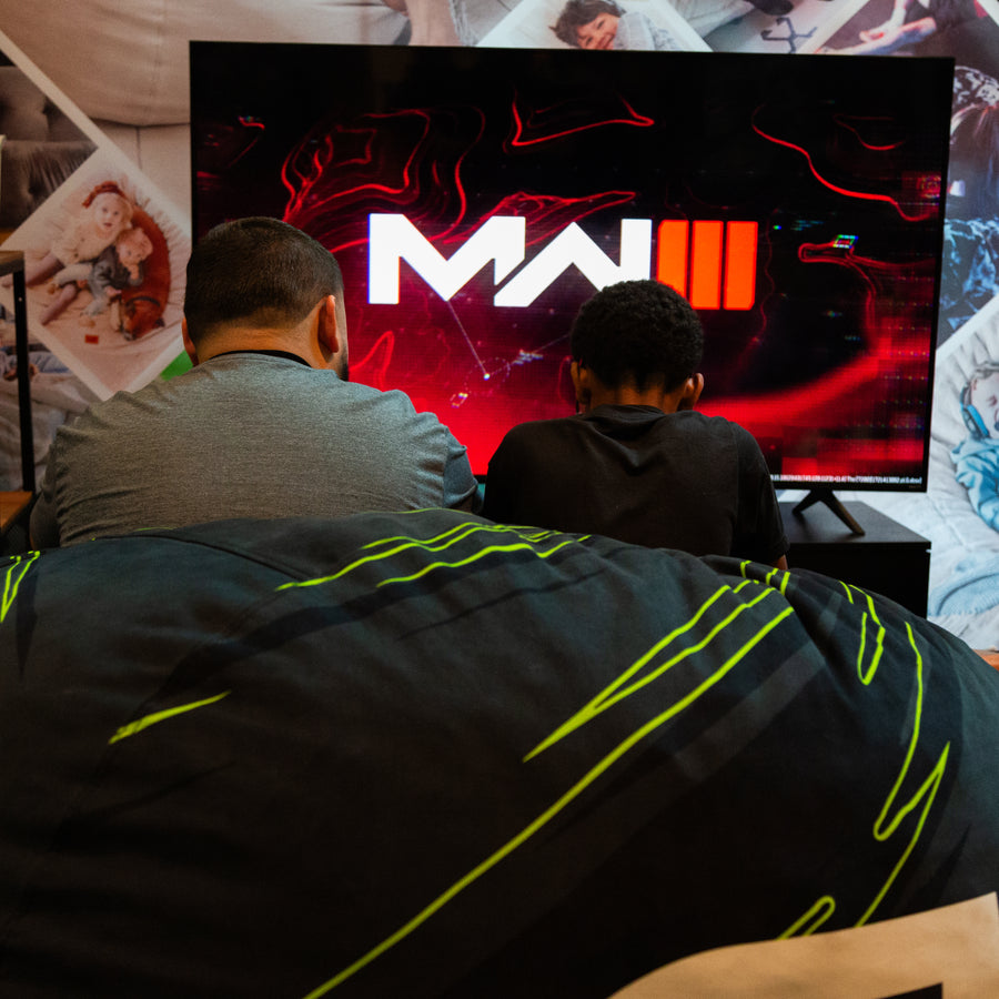 Father and son gaming in front of a television screen displaying a logo with the letter.
