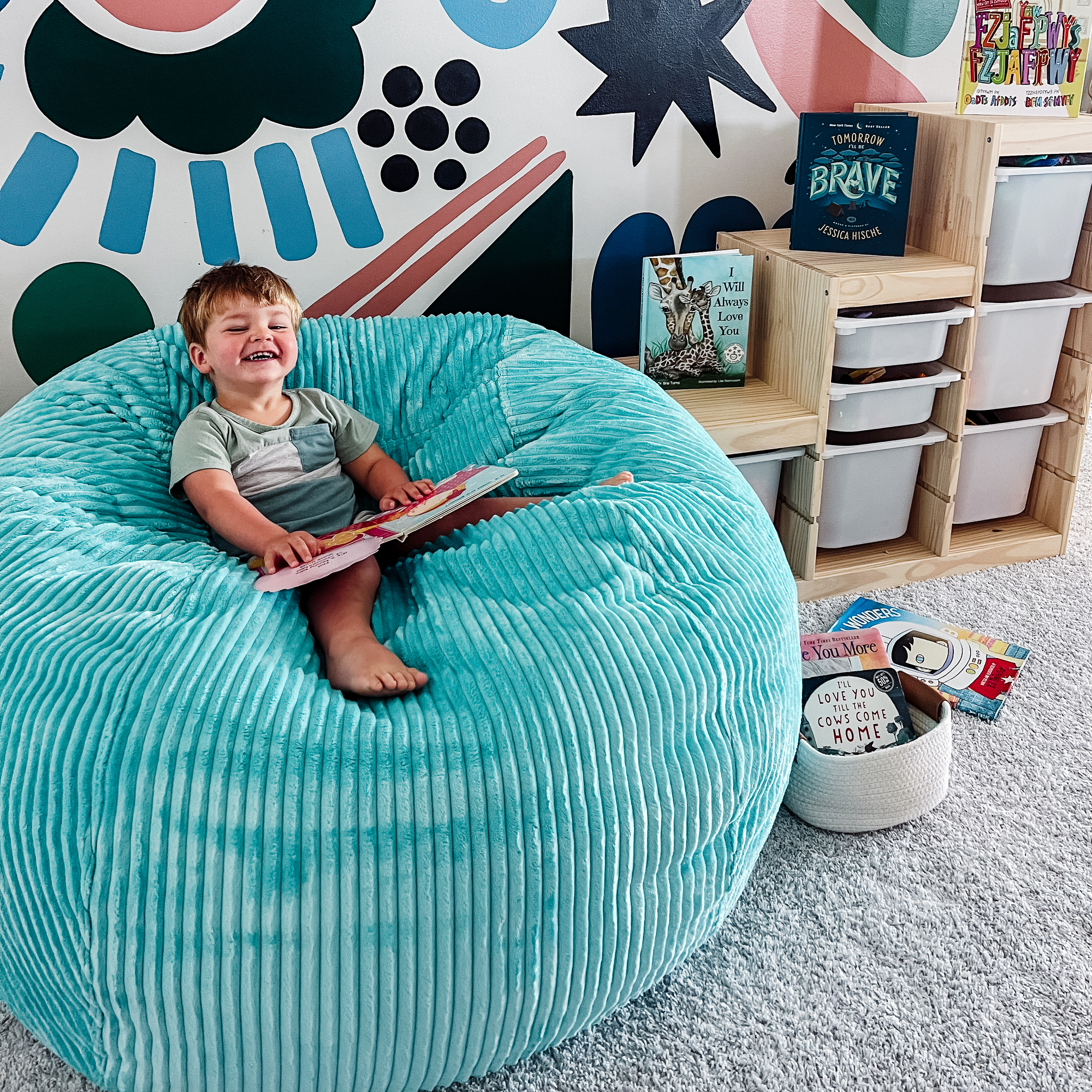 Happy boy holding book, sitting on bean bag in a child's playroom.