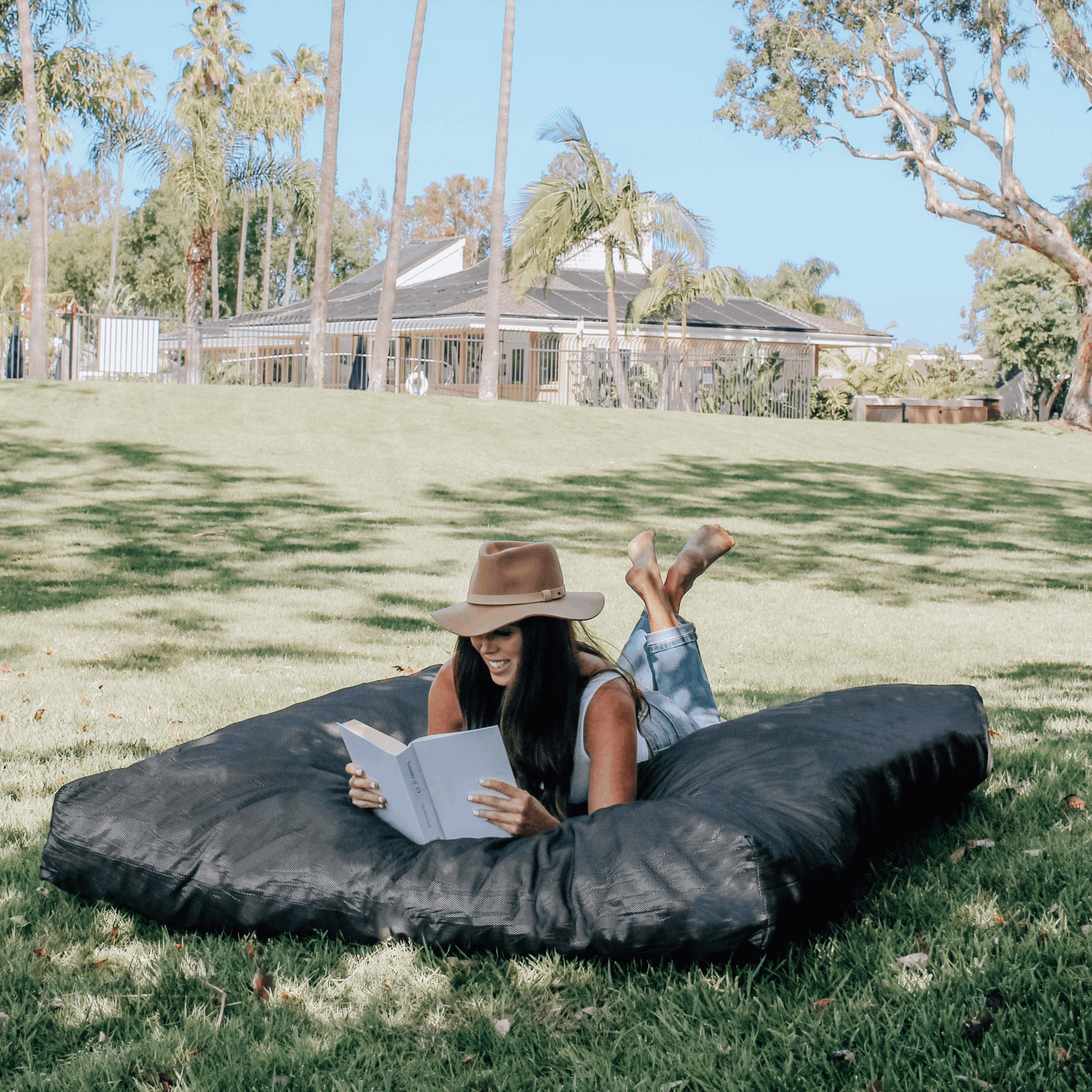 A woman reads a book on a cordaroys outdoor bean bag in bed form. 