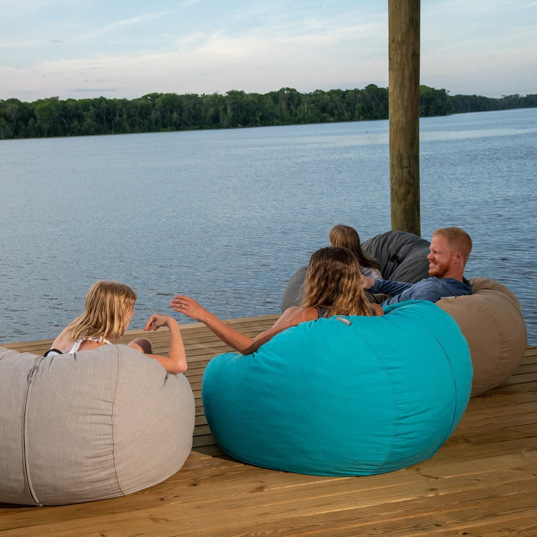 A family of three sits in outdoor bean bags on a dock. 